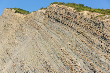 Shale, layered rocks with green vegetation at the top against the blue sky.