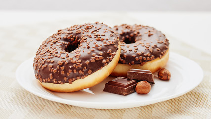 Glazed donut with chocolate and nuts on white plate