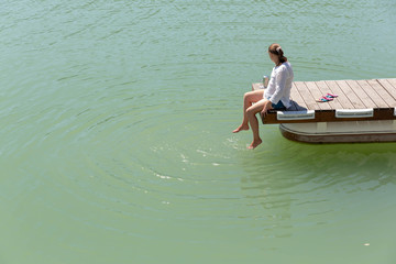 A young girl sitting on the dock and wet in the water of the lake legs.
