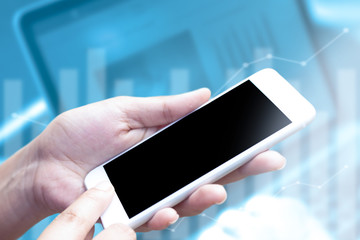 Close-up hand using mobile phone with blank display on laptop and graph background blurred. Concept is technology of business and financial.