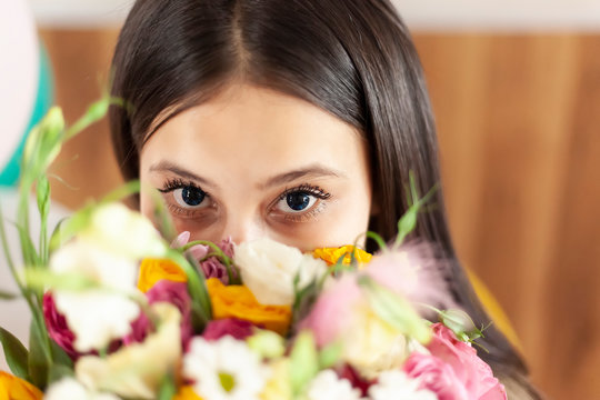 Attractive middle-eastern girl with beautiful eyes looking into the camera from behind flowers bouquet