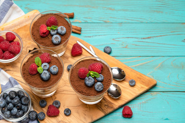 Classic tiramisu dessert with blueberries and strawberries in a glass cup and savoiardi cookies on wooden background