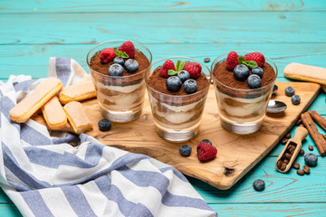 Classic tiramisu dessert with blueberries and strawberries in a glass cup and savoiardi cookies on wooden background