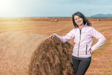 Naklejka na ściany i meble Happy beautiful brunette woman touching a round hay bale in the countryside