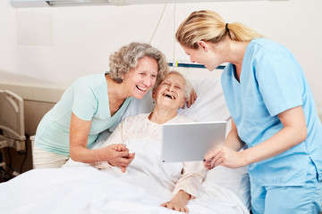 Pflegekraft zeigt Senior Frau einen Tablet PC