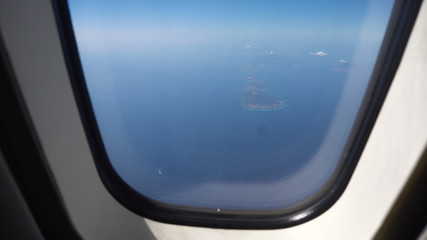 Airplane flying over blue sea and island. Looking through window aircraft during flight