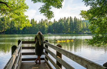 Woman enjoying lake view in forest standing on wooden pier