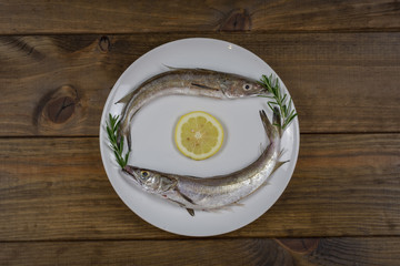 Pescado fresco sobre plato blanco en mesa de madera con utensilios de cocina.