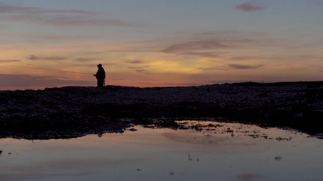 Silhouette of a fisherman fishing alone during sunset.