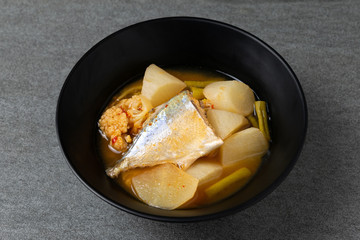 Sour curry with papaya and half fish in black bowl on the concrete table.