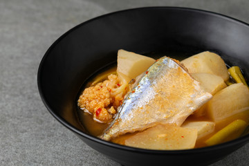 Sour curry with papaya and half fish in black bowl on the concrete table.