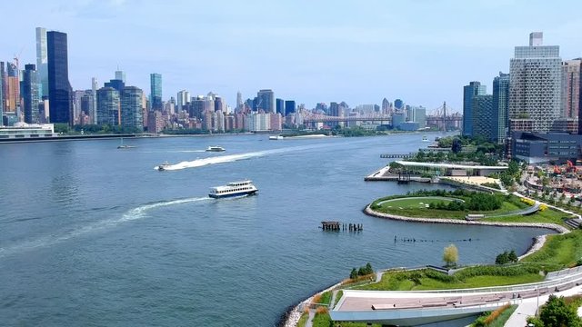 Scrolling up from a park revealing the New York CIty skyline and moving water taxis and private boats. Ed Koch Queensboro Bridge also revealed in the background.