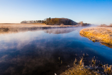 Mist over blue river curve on sunny morning. Beautiful landscape in countryside. Temperature drop concept