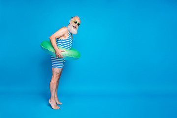 Full length profile side photo of funky grandfather ready to jump hold green lifesaver wear eyeglasses spectacles eyewear striped bathing suit isolated over blue background © deagreez