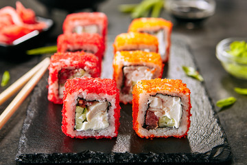 Macro shot of chicken maki sushi rolls with rice, cream cheese, chicken fillet, tomato, cucumber, red flying fish caviar and nori. Fresh tory teriyaki uramaki roll on black stone background closeup © Ryzhkov