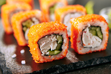 Macro shot of california maki sushi rolls with rice, cream cheese, imitation crab meat, cucumber, orange flying fish caviar and nori. Fresh crab roll on black stone background closeup