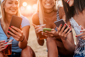 Close up of women drinking beer and using mobile phone at music festival
