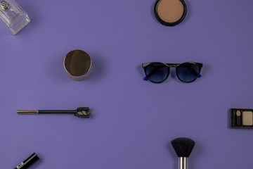 Elementos de maquillaje y moda de mujer sobre fondo violeta, pincel, brocha, corrector de ojos, pintalabios