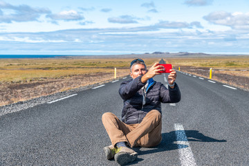 Fototapeta premium Traveller man sitting on the road taking a selfie. Strength and independence. Tourism, freedom and holiday concept