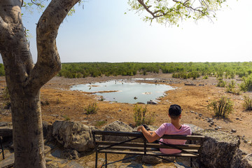 Tourist waits for wildlife at the Moringa waterhole near Halali, Etosha, Namibia - obrazy, fototapety, plakaty