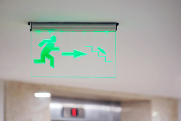 green evacuation direction sign on ceiling