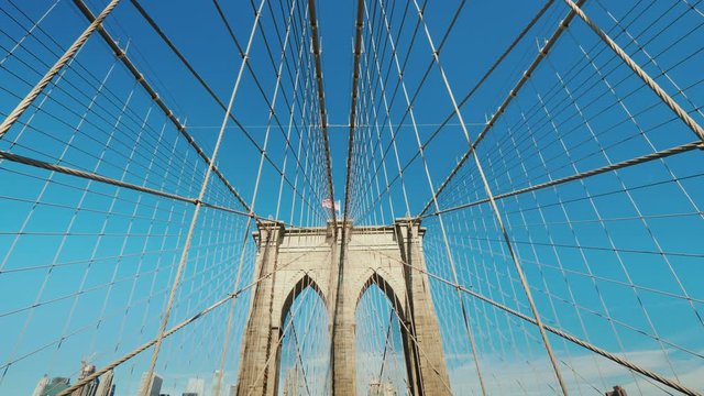 Wide angle shot: Walk on the Brooklyn Bridge. Pylons and ropes of the bridge against the serene blue sky. Pov video