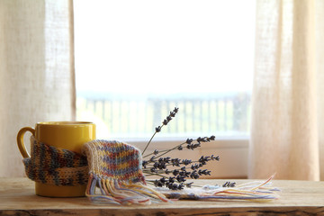yellow mug in a knitted scarf and a bouquet of flowers on a window background. cozy coffee with lavender flavor