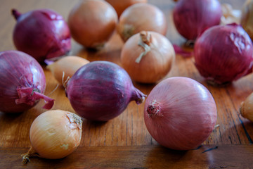 Whole brown and red onions on wooden board, selective focus