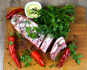  Ribs of pork raw meat on a wooden board next to herbs and chili peppers, oil and vinegar.     