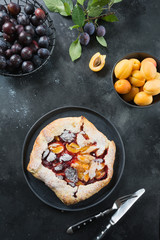 Homemade pie galette with plum and apricot on black table.