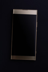 Gold colored smartphone with blank screen closeup flat on black background, top view