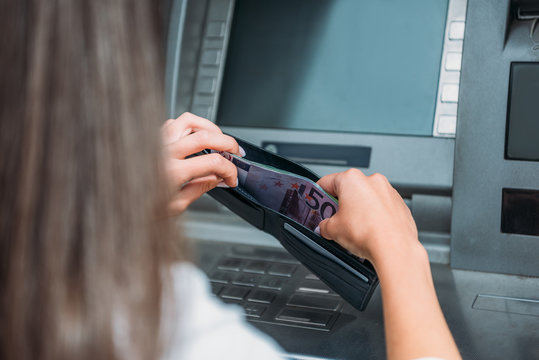 cropped view of woman putting money in wallet near atm machine