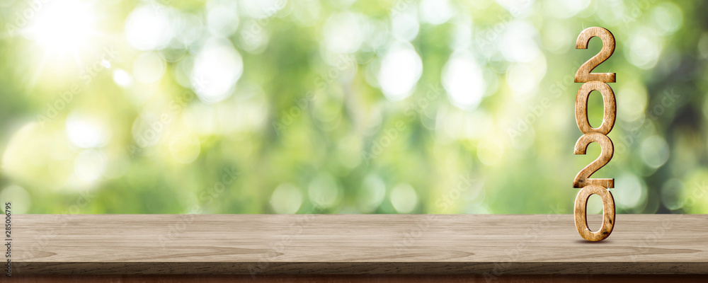 Poster new year 2020 wood number (3d rendering) on wooden table at blur abstract green tree bokeh backgroun