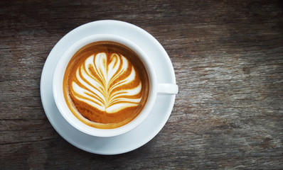 Hot latte art coffee in white mug top view on rustic wooden table with copy space on the right side.