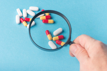 Concept - pharmaceutical testing, testing of medicines, magnifying glass, tablets on a blue background. Doping control.
