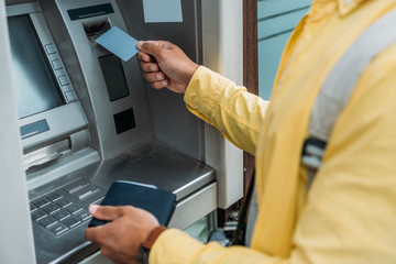 cropped view of mixed race man putting credit card in atm machine while holding wallet