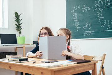 Schoolgirls hiding behind book sitting in a classroom