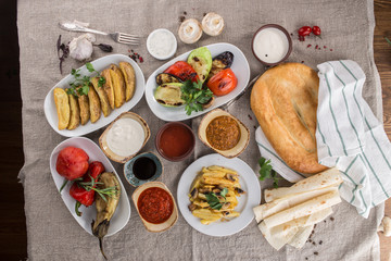 Grilled vegetables, potato wedges, potato with mushroom, different sauces and bread on rustic tablecloth