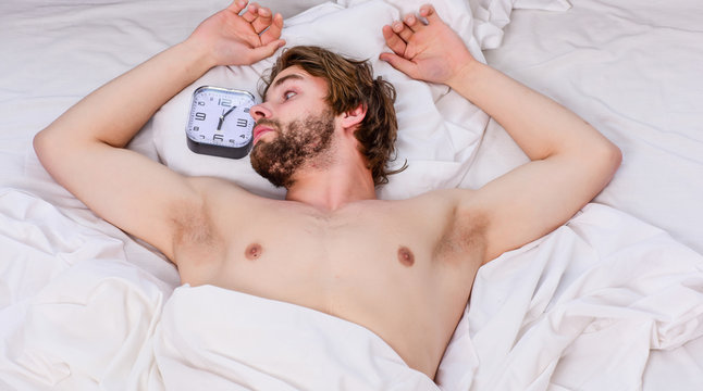 Man eyes are closed with relaxation. Cheerful young man is waking up after sleeping in the morning. Top view of sexy muscular young man sleeping in bed.
