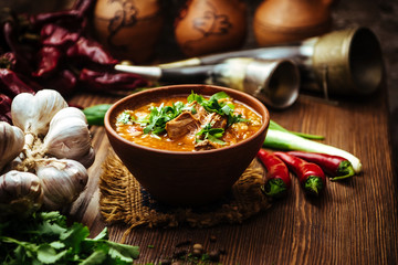 Kharcho soup with fresh parsley on a wooden background with fresh vegetables onions and garlic. Traditional georgian meat soup - obrazy, fototapety, plakaty