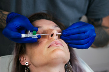 Portrait of a woman getting her nose pierced. Man showing a process of piercing nose with steril...