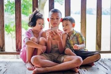 Three children sit and watch the smartphone happily. young boys and girls with cellphone communication. on the terrace of their house. to see today's children addictive technology.