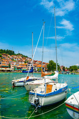 Fototapeta na wymiar North macedonia. Ohrid. Different sail boats beside dock on lake and houses on hill on background