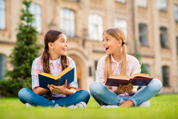 Fototapeta na wymiar Portrait of two nice attractive cute cheerful cheery glad brainy diligent knowledgeable intelligent pre-teen girls sitting on green grass spending day weekend reading outdoor
