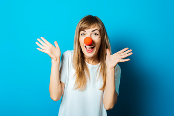 Beautiful young woman in a white T-shirt and a red clown nose smiles and makes hand gestures on a...