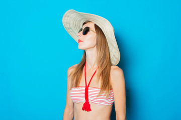 Young woman in a swimsuit, glasses and a wide-brimmed hat on a blue background. Concept of vacation, summer, vacation at sea
