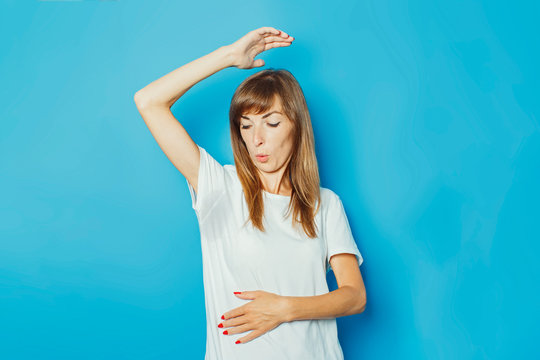 Young girl in a white T-shirt with wet armpits from sweat on a blue background. Concept of excessive sweating, heat, deodorant