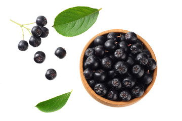 Chokeberry in wooden bowl with green leaves isolated on white background. Black aronia. Top view.