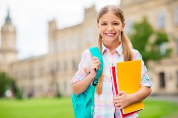 Portrait of charming child holding books smiling wearing checkered plaid t-shirt standing outdoors