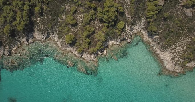 Aerial view of small beach with turquoise water next to rocks and trees in the area of Agia Paraskevi Halkidiki, Greece. View from drone